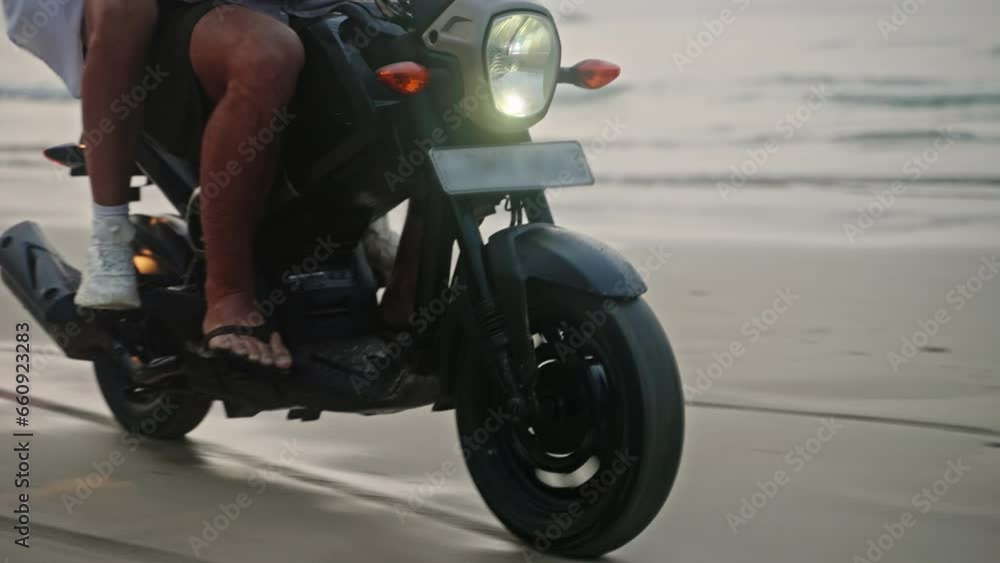 Travel couple ride motorcycle along sea beach on sunrise. Intraframe installation from people to wheels . Tourists drive rented motorbike on ocean coastline. Woman hugs man, spreads arms riding a bike Travel couple ride motorcycle along sea beach on sunrise. Intraframe installation from people to wheels . Tourists drive rented motorbike on ocean coastline. Woman hugs man, spreads arms riding a bike