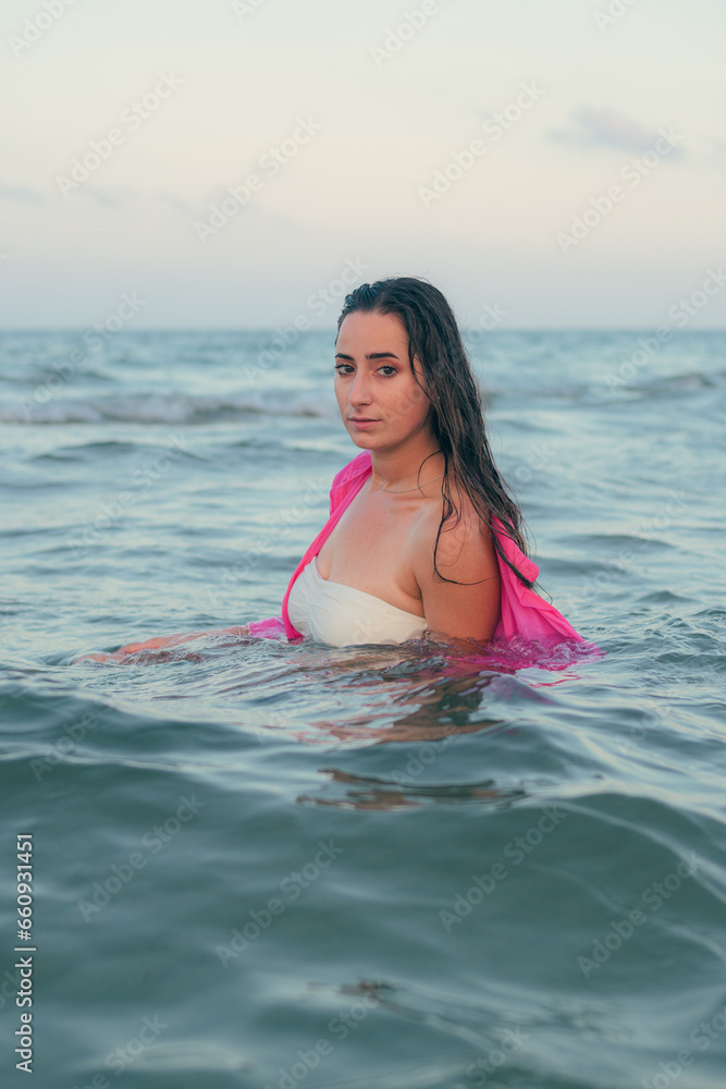 Young beautiful woman poses with the sea in the background at sunset