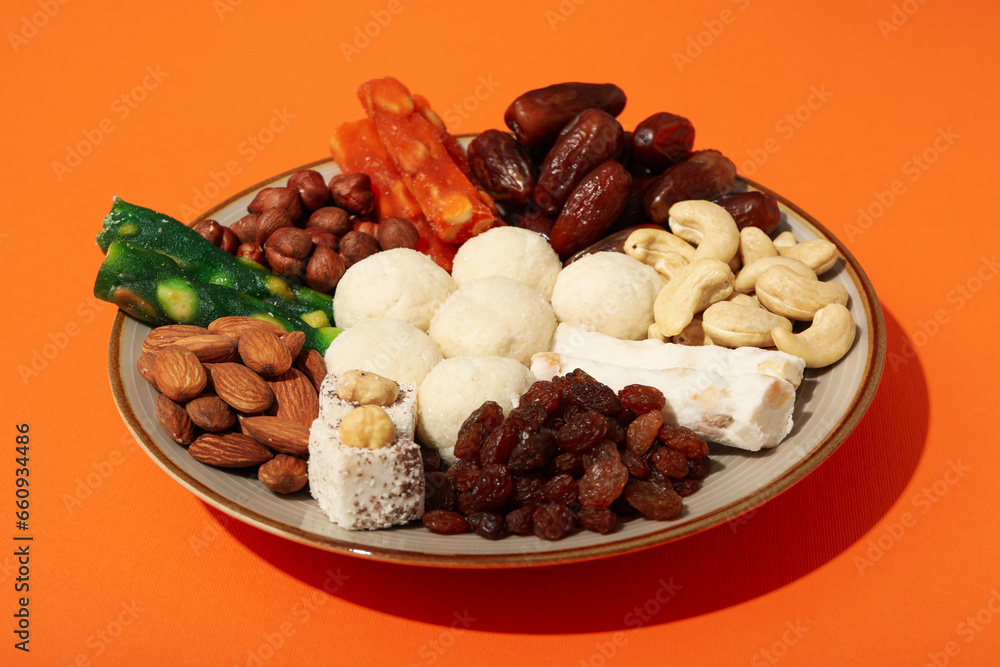 Plate with nuts and sweets on orange background, close up Plate with nuts and sweets on orange background, close up