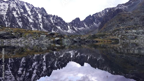 Beauty that cannot be described in words. Reflection of snow-covered acute peaks (sawback) in quiet mountain lake (subnival belt) combines peace and thrill. God's country. Sayan Mountains, Siberia photo