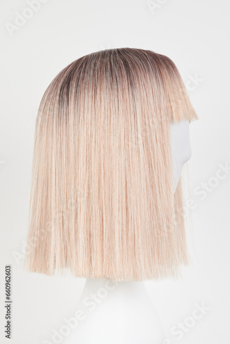 Natural looking blonde fair wig on white mannequin head. Short hair cut on the plastic wig holder isolated on white background, side view.