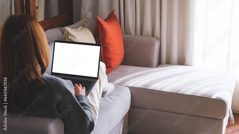 Mockup image of a woman working and typing on laptop computer with blank screen while sitting on sofa at home Mockup image of a woman working and typing on laptop computer with blank screen while sitting on sofa at home