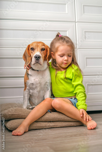 The child is sitting hugging an obedient kind dog of the Beagle breed.
