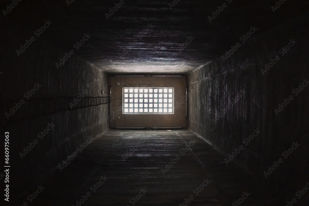 Light behind barred window in the dark prison cell - empty jail interior with grey concrete walls
