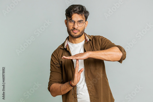 Tired serious upset Indian young man showing time out gesture, limit or stop sign, no pressure, I need more time, take a break, relax, rest, help. Arabian guy isolated on gray studio background