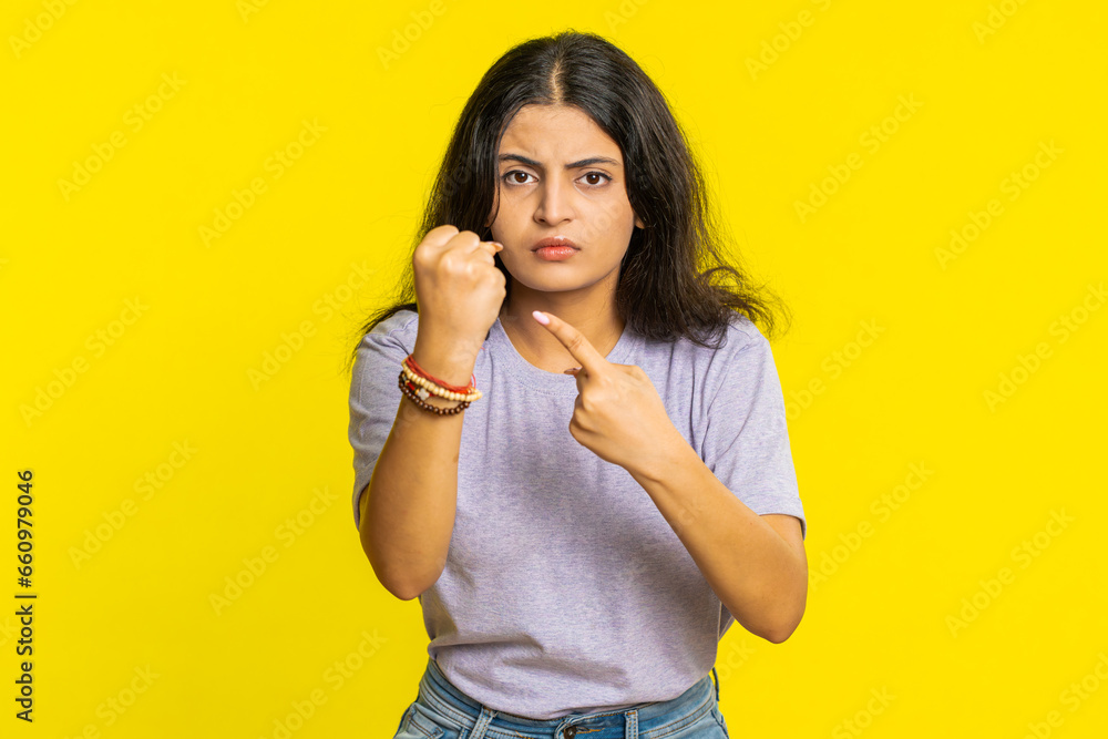 Aggressive angry Indian young woman trying to fight at camera, shaking fist, boxing with expression, punishment, threaten, bullying, abuse, mad fury. Arabian girl isolated on yellow studio background Aggressive angry Indian young woman trying to fight at camera, shaking fist, boxing with expression, punishment, threaten, bullying, abuse, mad fury. Arabian girl isolated on yellow studio background