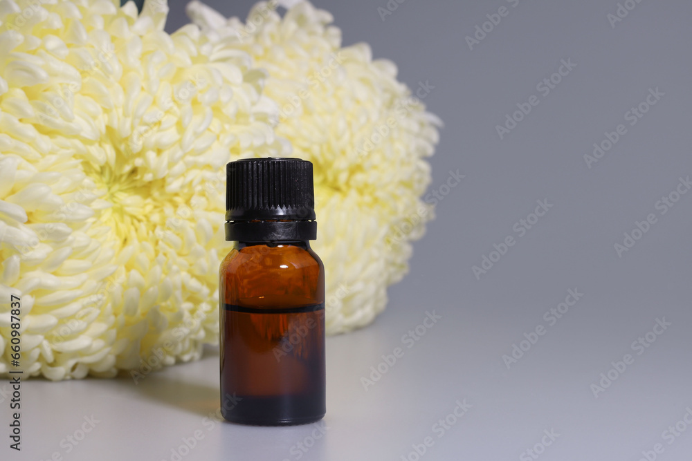 a transparent brown bottle with liquid stands next to white asters flowers a transparent brown bottle with liquid stands next to white asters flowers
