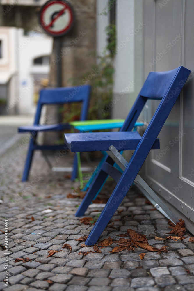 Blue chairs with leaves on the ground on a wet autumn day