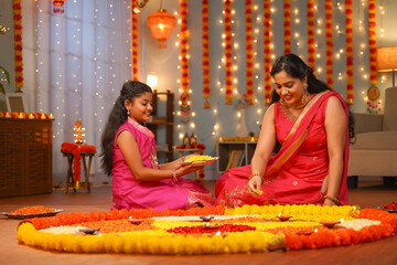 focus on kid,Happy Indian young Mother with daughter preparing Diwali rangoli for celebration - concept of home decoration, family bonding and religious custom.