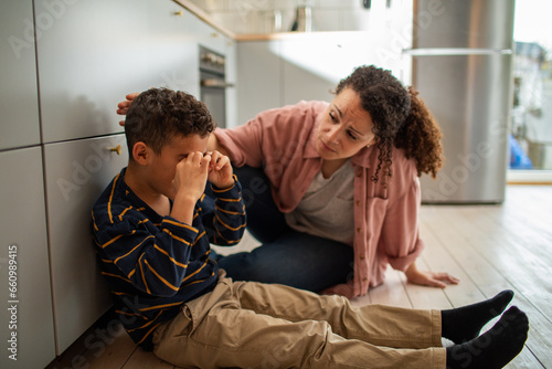 Young mixed mother comforting her crying son on the floor at home photo