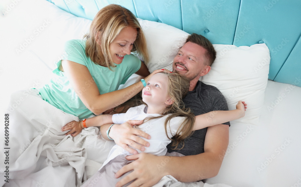 Parents and child lie in bed laughing and hugging. Joint family leisure concept