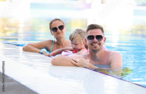 Smiling parents with their child are standing near side of pool. Family travel water park concept © H_Ko