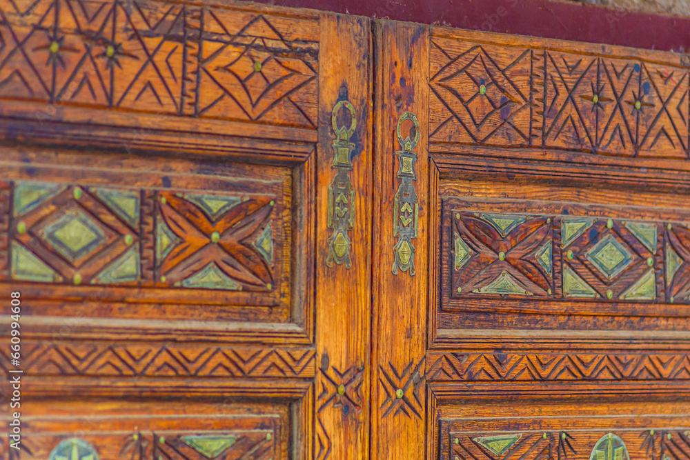 Big old wooden door decorated with various symbolic signs carved directly on the canvas of massif. Example of exterior and interior decoration of entrance lobbies in different cultures around world