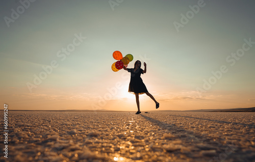 Silhouette of woman holding balloons while standing at beach against sky during sunset      