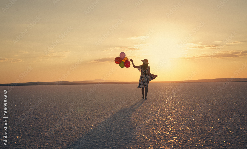 Silhouette of woman holding balloons while standing at beach against sky during sunset      