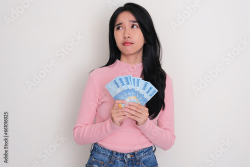 A woman looking to upper right corner with confused expression while holding money photo