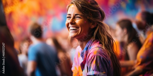 A beautiful girl smiles happily against a bright backdrop, a European-looking blonde in paint-splattered clothing, a happy artist smiling broadly.