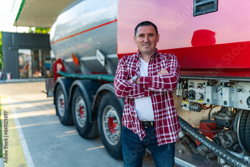 a male tanker or truck driver poses next to his vehicle at a gas station, casually dressed and ready to go
