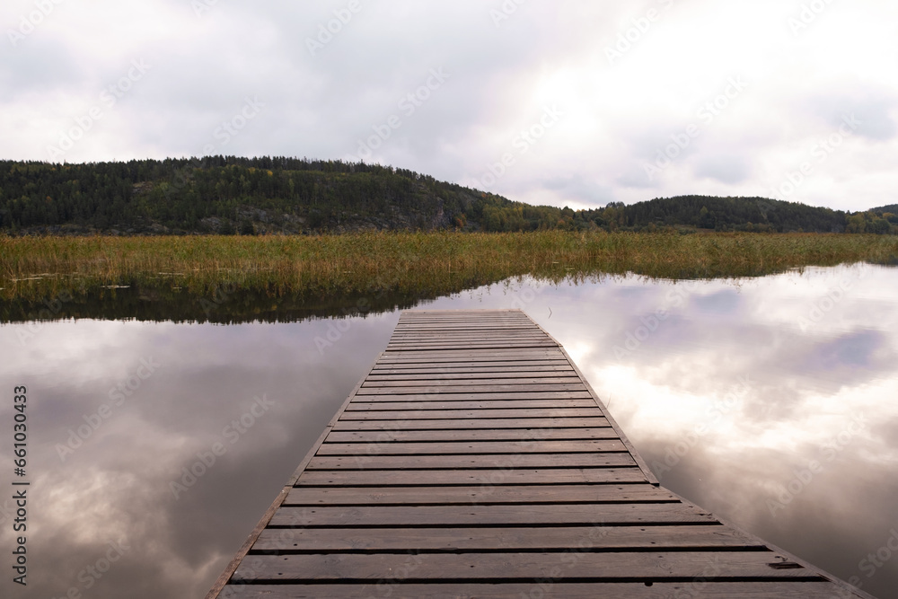 Fototapeta premium Wooden pier on a calm windless lake in the early morning. Cloudy sky.