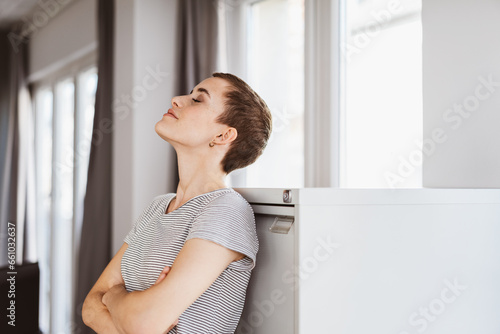 Office Oasis: Young Modern Woman with Short Hair Finds Serenity Leaning Against Cabinet with Closed Eyes