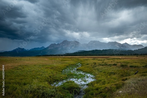 a field covered in grass and a river running under a stormy sky