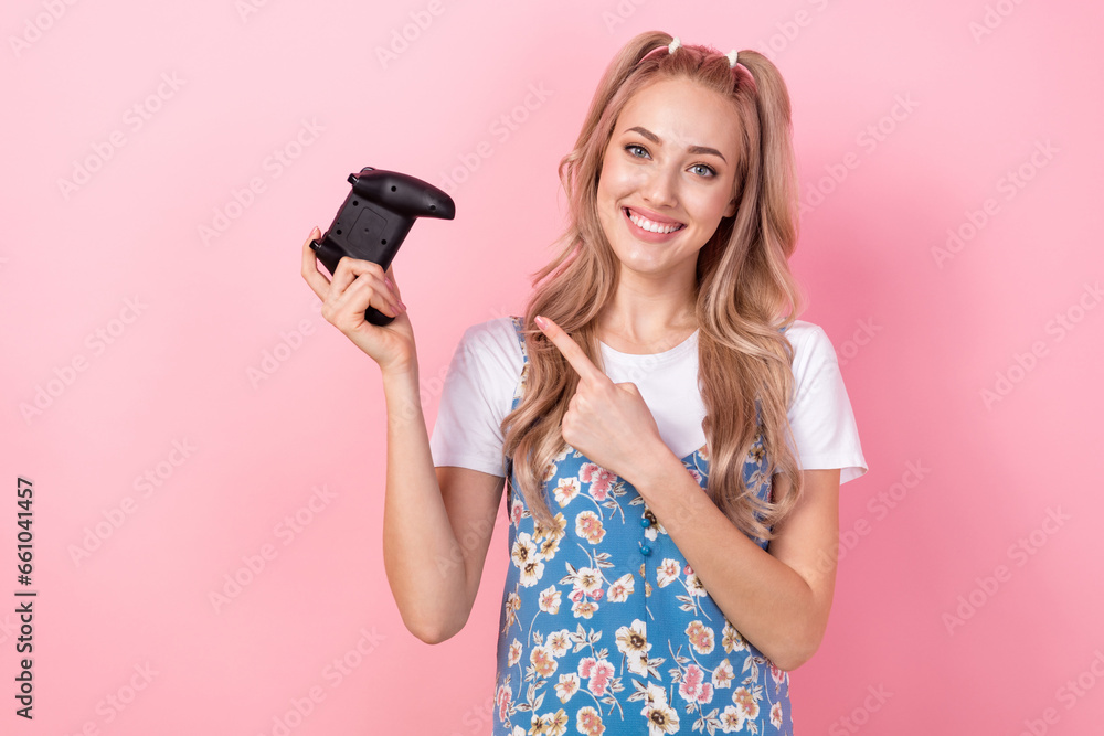 Portrait of satisfied girl with ponytails wear t-shirt under dress directing at playstation joystick isolated on pink color background Portrait of satisfied girl with ponytails wear t-shirt under dress directing at playstation joystick isolated on pink color background