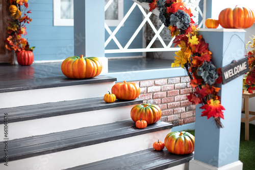 Residential house decorated for Halloween holiday. Different colored pumpkins in front door On Wooden Steps. Porch of yard decorated with orange pumpkins in autumn. Thanksgiving. Halloween outside.	
