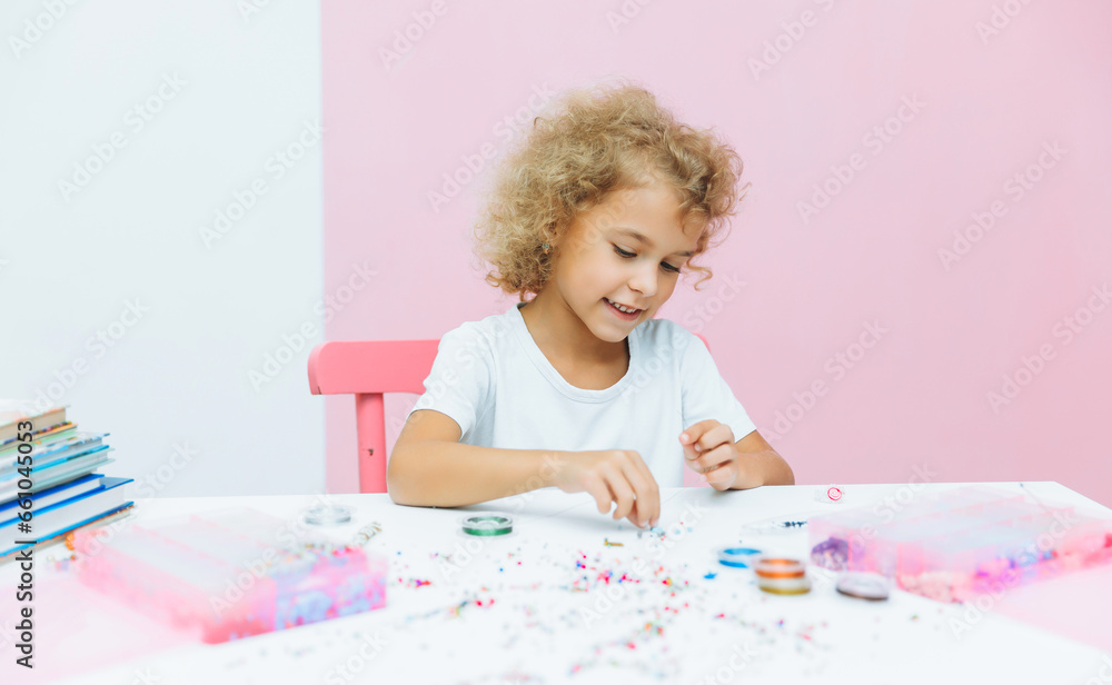 Cute little blonde girl making bead jewelry at a table in the room Cute little blonde girl making bead jewelry at a table in the room