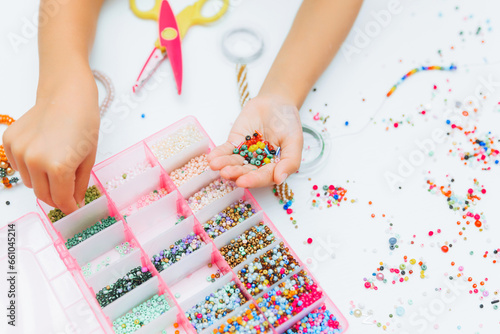 Obraz na plátně Cute little blonde girl making bead jewelry at a table in the room