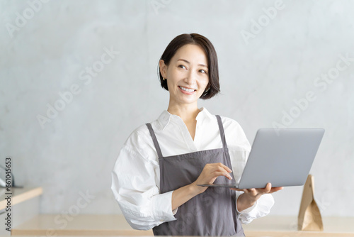 ノートパソコンを持つエプロン姿の女性