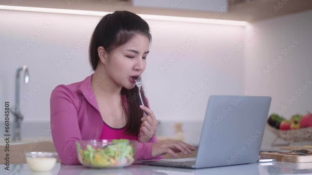 sporty young Asian woman in sportswear looking at laptop and eating vegetables Salad in the kitchen interior, Healthy diet and sport concept. sporty young Asian woman in sportswear looking at laptop and eating vegetables Salad in the kitchen interior, Healthy diet and sport concept.