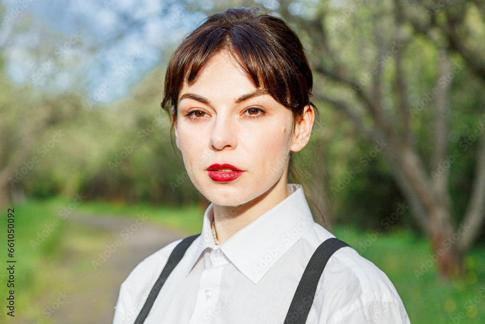 A beautiful girl in a white shirt, in black trousers with suspenders against the background of the sky and green grass A beautiful girl in a white shirt, in black trousers with suspenders against the background of the sky and green grass