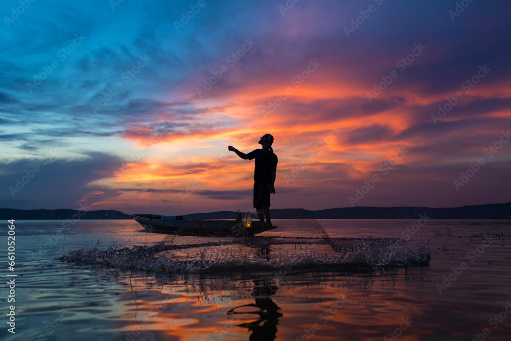 Silhouette of Asian fisherman throwing fishing nets during sunrise on boats on lake in the morning.