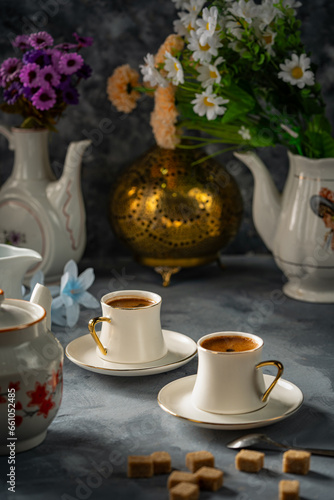 Two cups of Turkish coffee on a gray ground and a group of white utensils and flowers