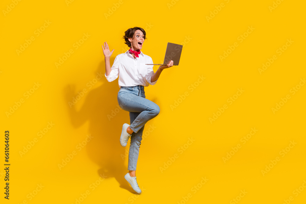 Full length photo of cheerful adorable girl wear trendy clothes speaking online macbook netbook isolated on yellow color background Full length photo of cheerful adorable girl wear trendy clothes speaking online macbook netbook isolated on yellow color background