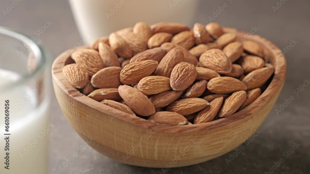 An almond nuts bowl is placed on a wooden table. Almonds and almond milk. An almond nuts bowl is placed on a wooden table. Almonds and almond milk.