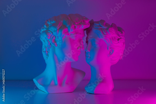 Two antique statue's heads in pink and blue colored neon light. Relationships of man and woman. Love, romance, kiss, tenderness. Modern design. Contemporary art. David and Aphrodite