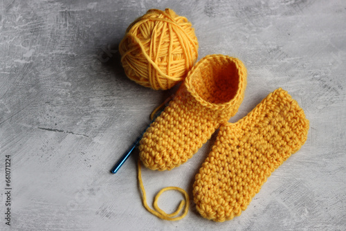 Cute crochet slippers made of organic thread close up photo. Handmade Christmas gift ideas. Grey textured background with copy space. Hobby and leisure concept. 