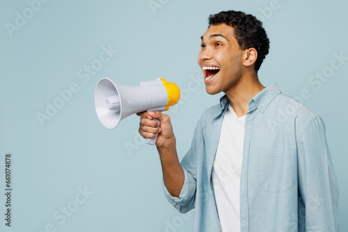 Side view young surpised man of African American ethnicity in shirt casual clothes hold in hand megaphone scream announces discounts sale Hurry up isolated on plain pastel light blue cyan background