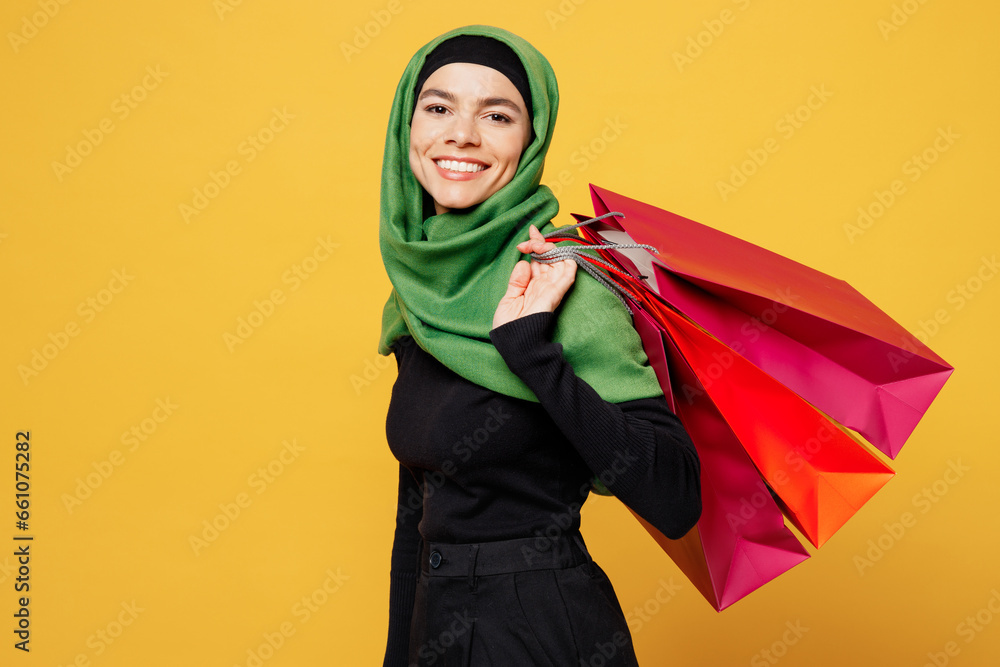 Side profile view young arab asian muslim woman wears green hijab abaya clothes hold shopping package bags look camera isolated on plain yellow background Black Friday sale buy day, uae islam concept Side profile view young arab asian muslim woman wears green hijab abaya clothes hold shopping package bags look camera isolated on plain yellow background Black Friday sale buy day, uae islam concept