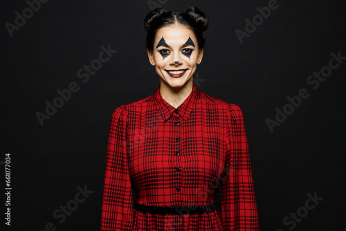 Young smiling cool woman with Halloween makeup face art mask wearing clown costume red dress looking camera isolated on plain solid black wall background studio portrait. Scary holiday party concept.