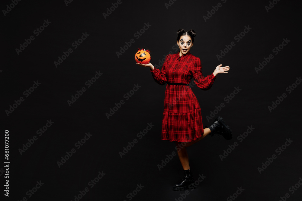 Full body young woman with Halloween makeup face art mask wear clown costume red dress hold Jack-o-Lantern carved pumpkin posing isolated on plain black background studio. Scary holiday party concept. Full body young woman with Halloween makeup face art mask wear clown costume red dress hold Jack-o-Lantern carved pumpkin posing isolated on plain black background studio. Scary holiday party concept.