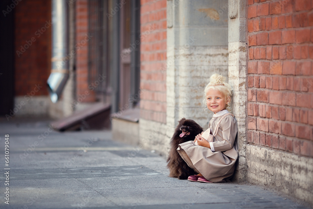 Little girl with blonde hair wearing dress with a dog on the city street 