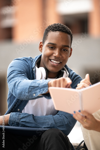 Young handsome guy wearing headphones pointing a notebook.Confident student sitting and reading notes with a colleague. © carlesiturbe