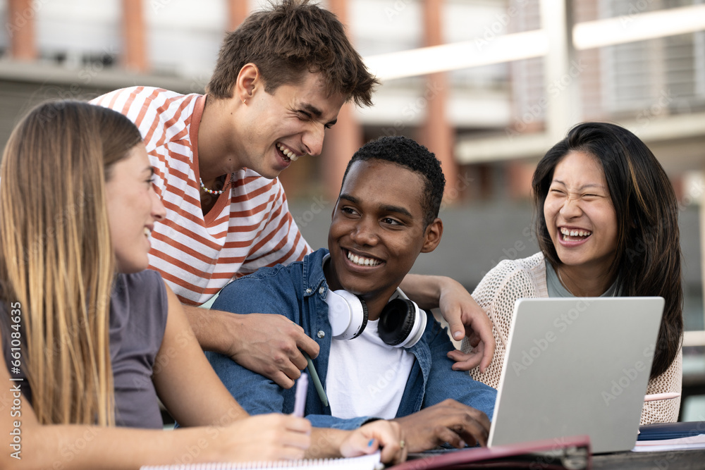 Multicultural group of people working together with a laptop.Young happy friends laughing outside using computer and notes. Multicultural group of people working together with a laptop.Young happy friends laughing outside using computer and notes.