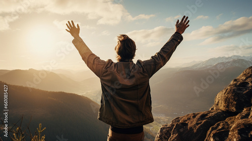 Positive man celebrating on mountain top, with arms raised up