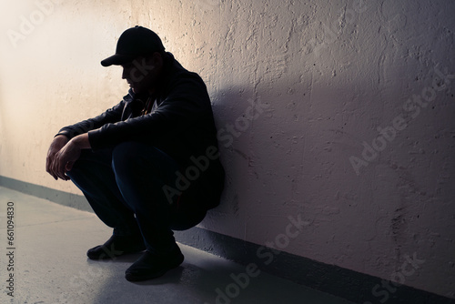 Man with trauma, shame or anxiety. Sad desperate young guy or teenage boy. Drug addiction or despair. Criminal outcast or homeless person with stress in dark. Silhouette of victim of discrimination.