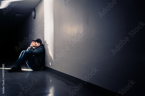 Sad man with trauma sitting on floor. Shame, guilt or sorrow. Desperate guy crying in dark corridor. Victim of loneliness or discrimination. Negative emotion or depression. Lonely outcast worrying. photo
