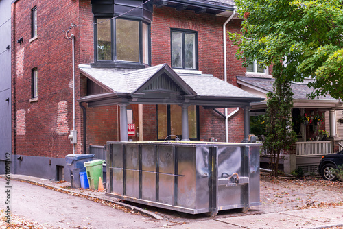 Photography A roll-off construction dumpster, black end view, outside a residential renovation project in an older neighourhood