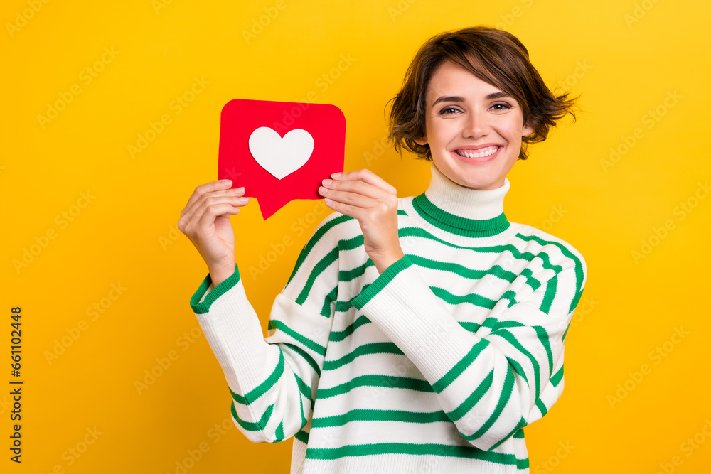 Photo of positive sweet lady wear striped pullover smiling rising heart like card isolated yellow color background Photo of positive sweet lady wear striped pullover smiling rising heart like card isolated yellow color background